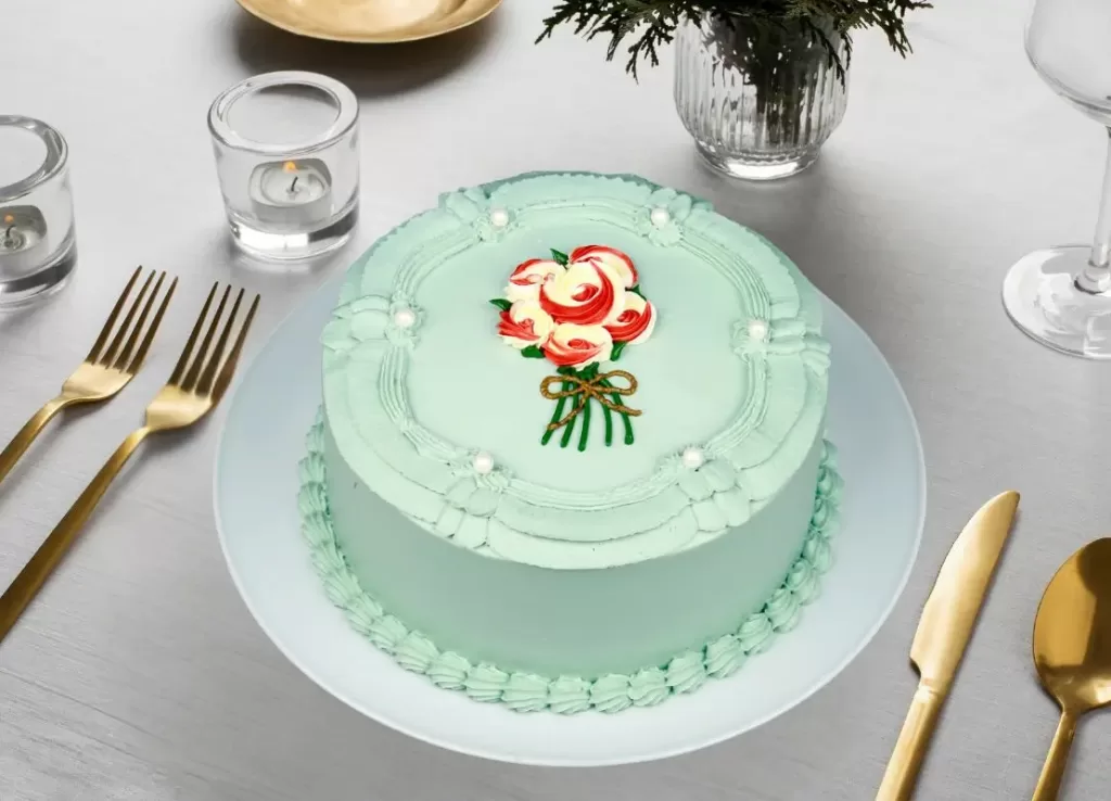 Elegant round cake with mint green cream cheese frosting, vintage piped border, and hand-painted floral bouquet design
