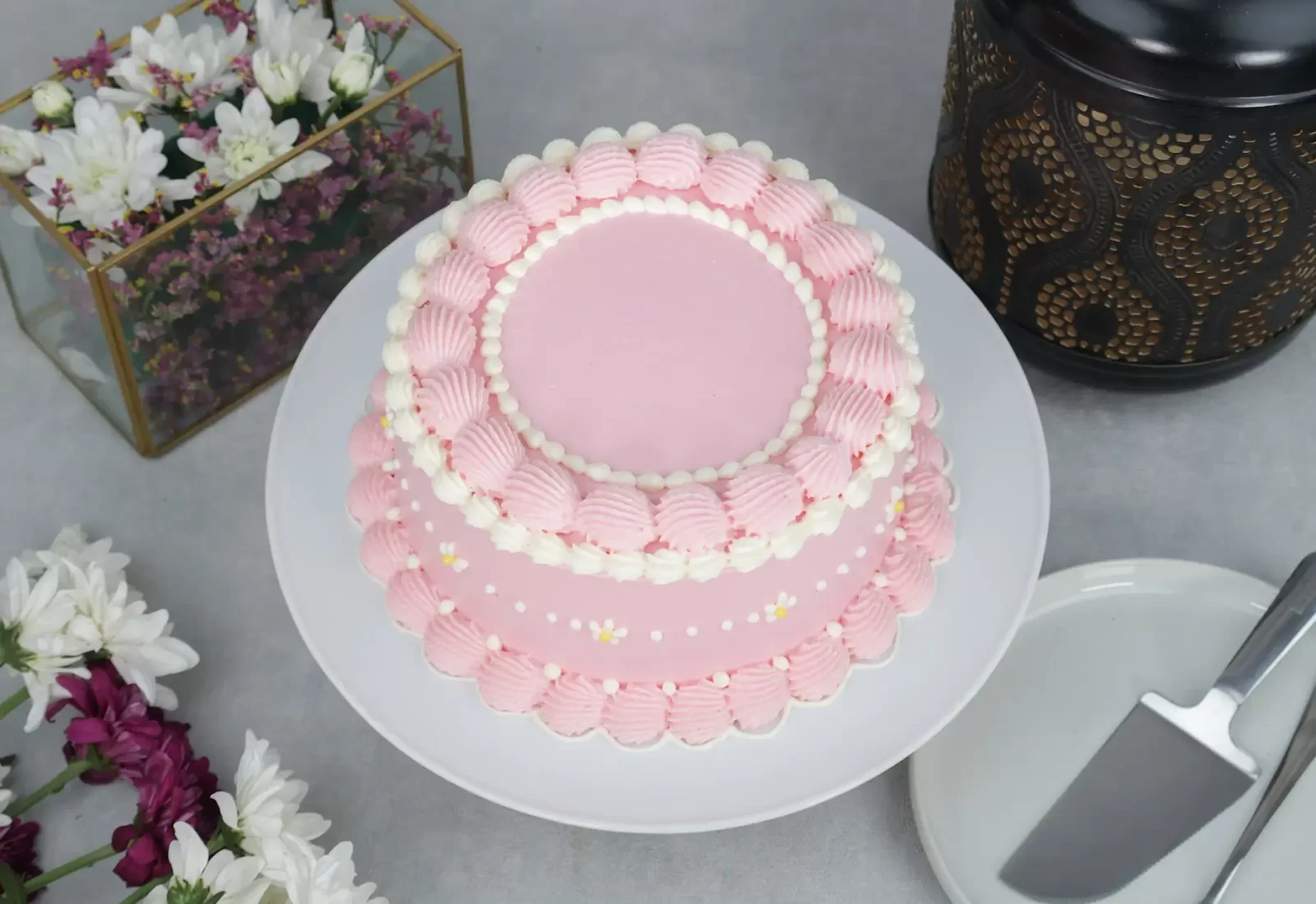 A pink cake on the platter with flowers on the side